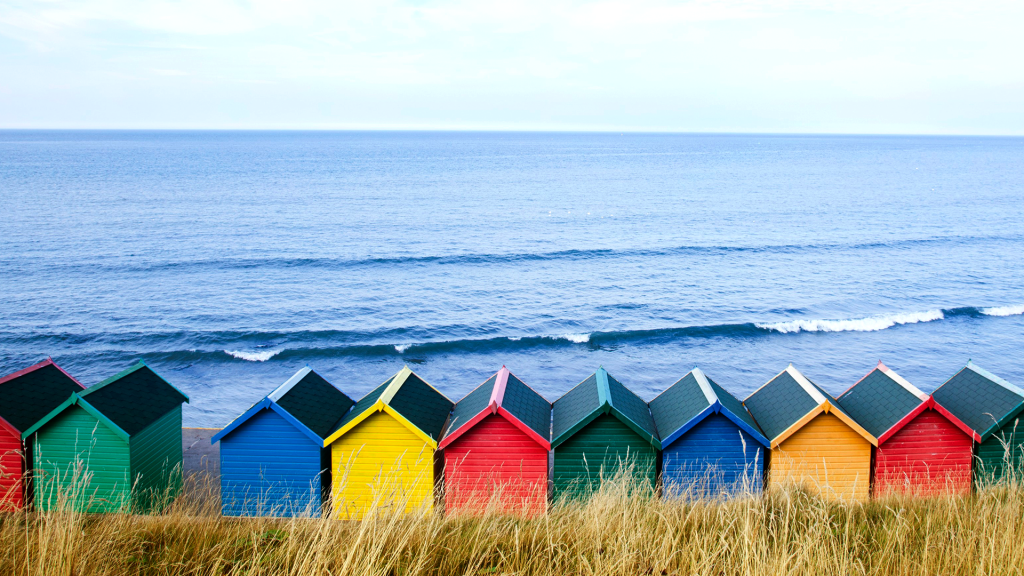 Colourful beach huts along the seafront, North Yorkshire, Whitby, England, UK