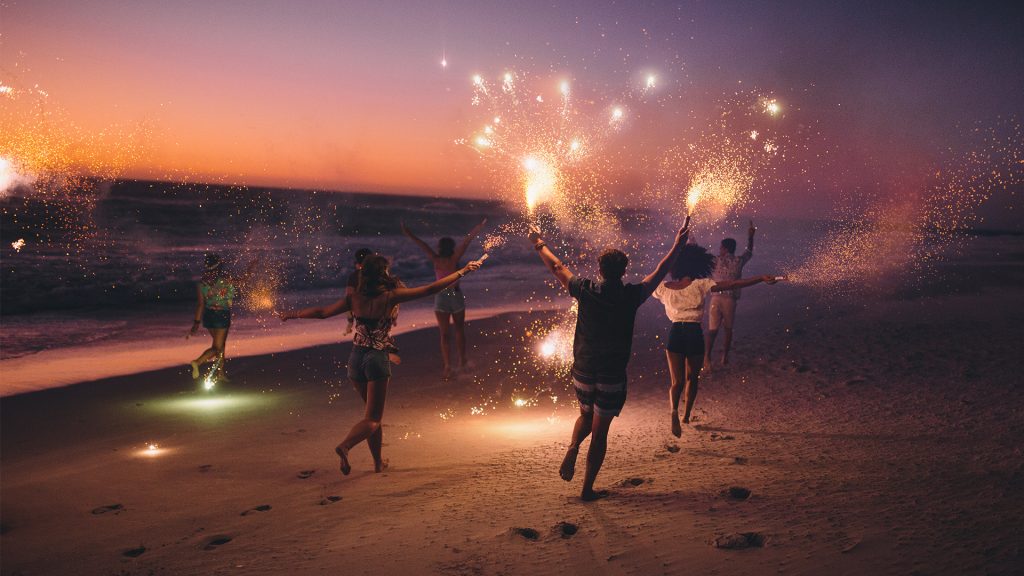 Friends running with fireworks on a beach after sunset