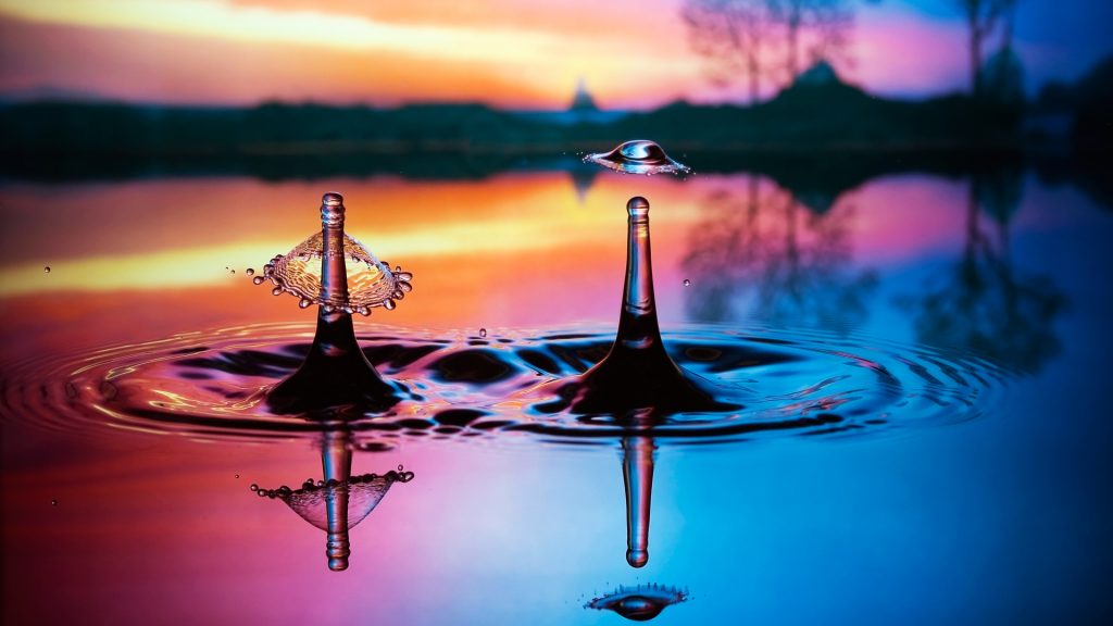 Double liquid art, water splashes reflecting on colorful pool outdoors at sunset