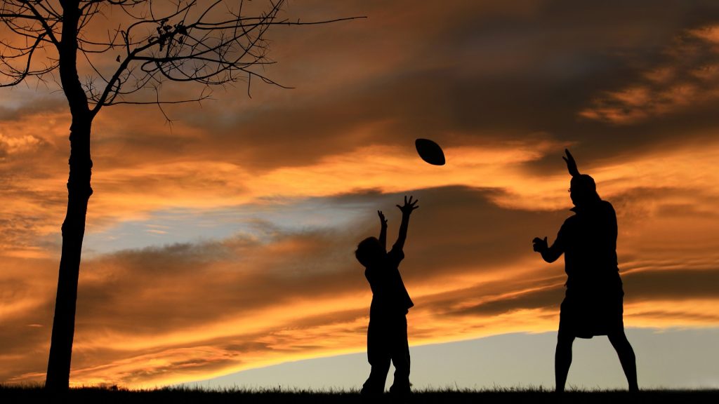 Silhouette of father playing football with his son