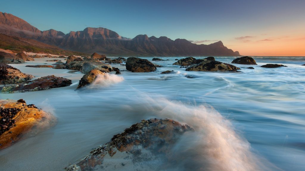 Water collides with coastal rocks at sunset over Kogel Bay in the Cape Province, South Africa