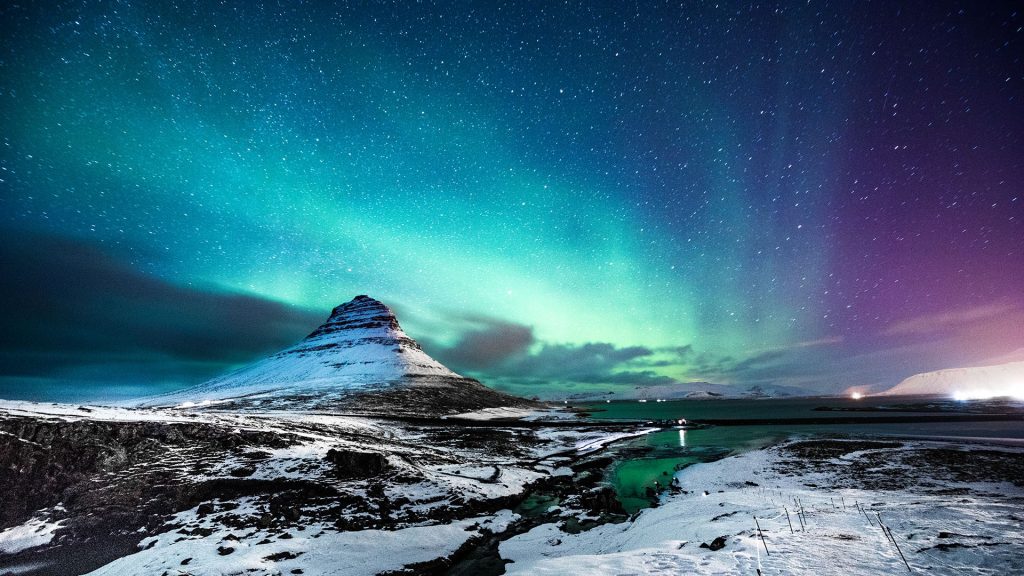 Northern lights at Mount Kirkjufell with a man passing by, Iceland