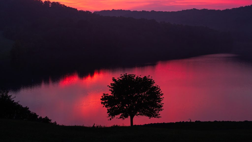 A colorful sunrise sky reflected on the waters of Grayson Lake reservoir, Kentucky, USA
