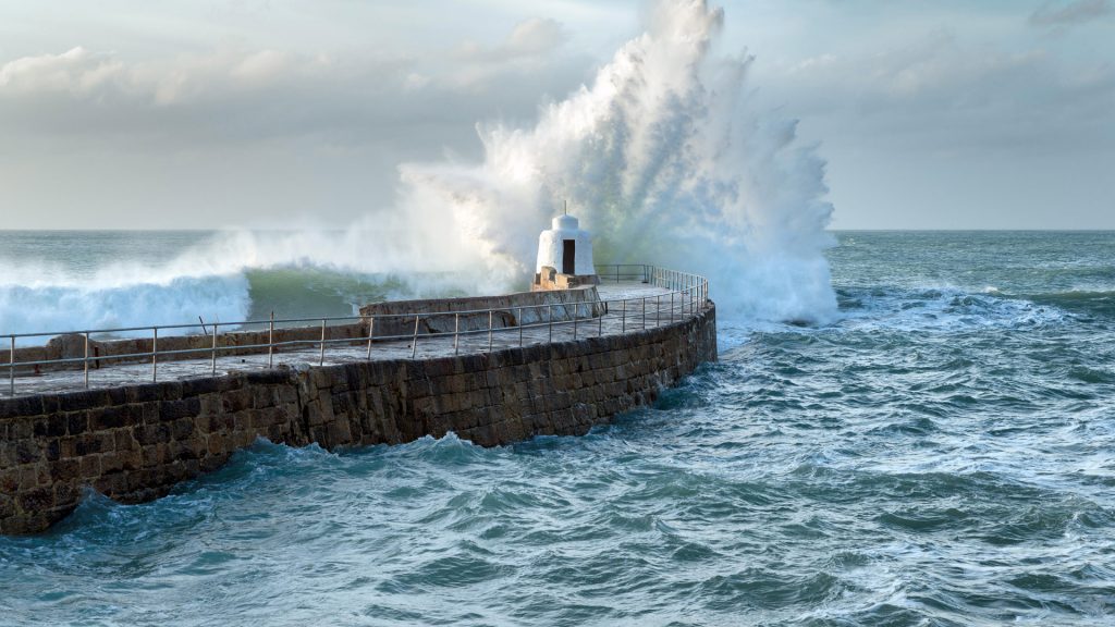 Waves crashing over the Monkey Hut on the stone pier, Portreath, Cornwall coast, England, UK