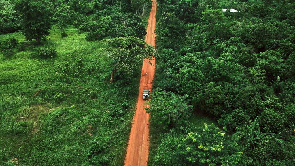 Aerial view of a car driving along dirt road through green jungle, Korhogo, Ivory Coast