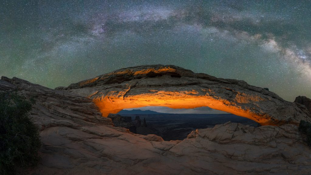 Milky Way Galaxy panorama over a lit Mesa Arch in Canyonlands National Park, Utah, USA
