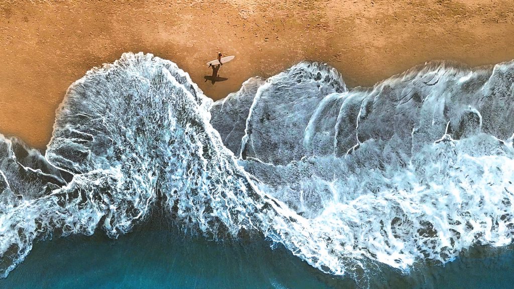 Surfer walking along on sunny summer day, ocean waves reach sandy beach, Bali, Indonesia