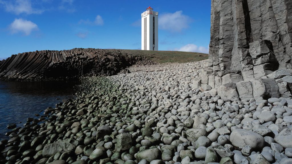 Kálfshamarsvík lighthouse at a pebble beach surrounded by basalt, Iceland