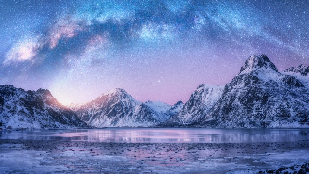 Milky Way above sea coast and snow covered mountains in winter night, Lofoten Islands, Norway