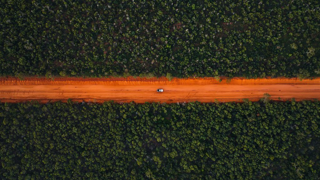 Off-road vehicle on an orange dirt road in a forest, Dampier Peninsula, Western Australia