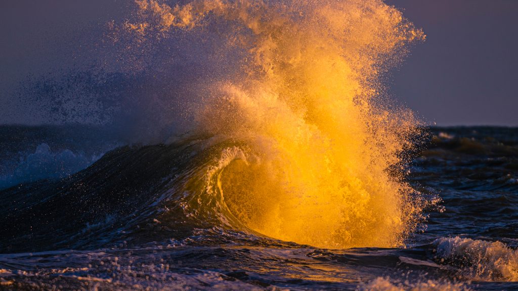 Wave rises and crashes off the tip of Cape Hatteras at sunset, North Carolina, USA