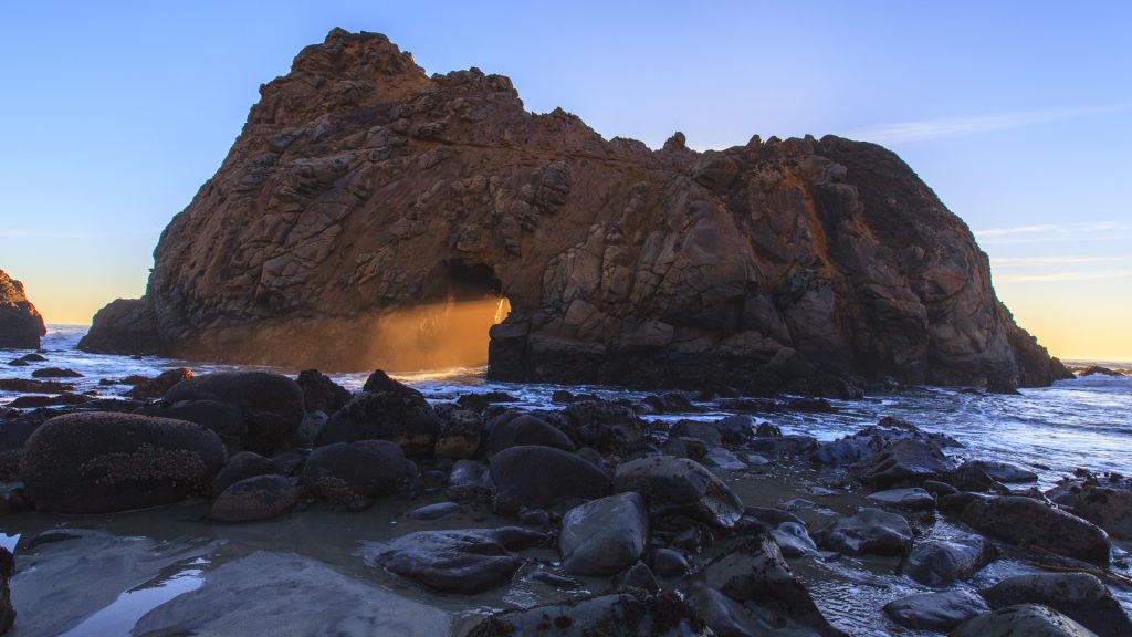 Sunbeams shining through rock formation at sunset on Pfeiffer Beach, California, USA